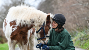 A skewbald pony named Blisland Boo Boo gently touching foreheads with a smiling horse sanctuary worker.